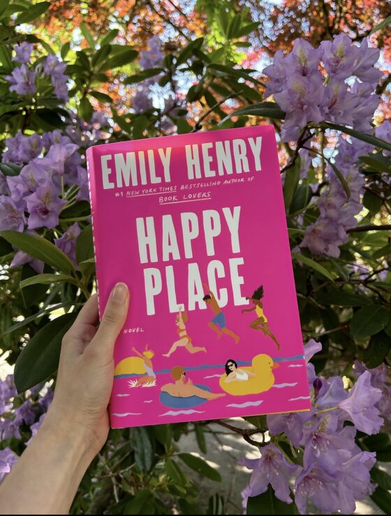 Happy Place being held up in front of pink flowers.