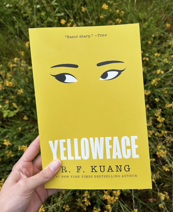 Yellowface being held up in front of yellow flowers