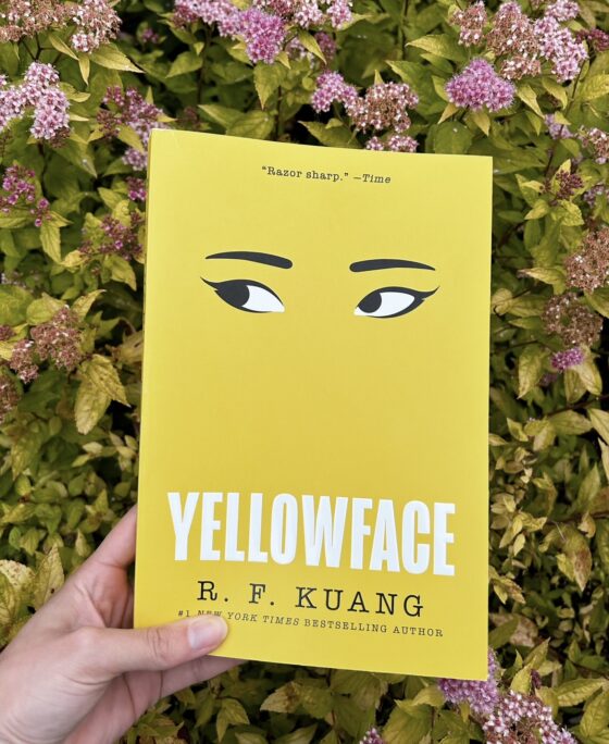 Yellowface being held up in front of pink flowers and yellow leaves