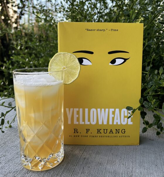 Yellowface sitting behind yellow bird cocktail with green plant in background.