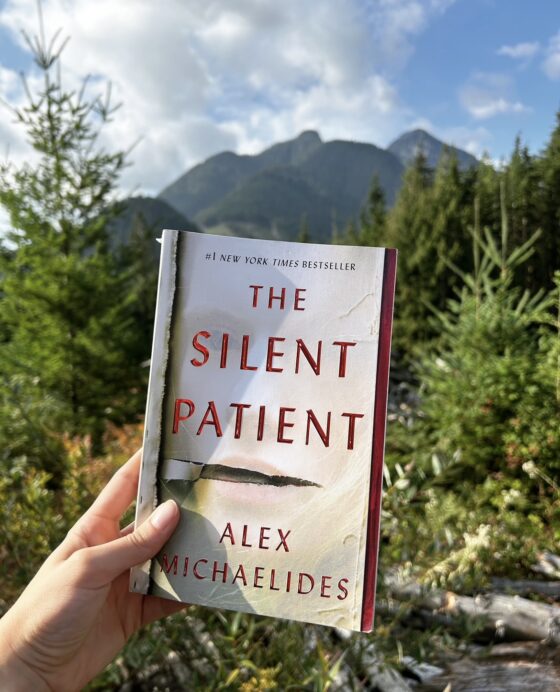 The Silent Patient held up in front of trees and mountains