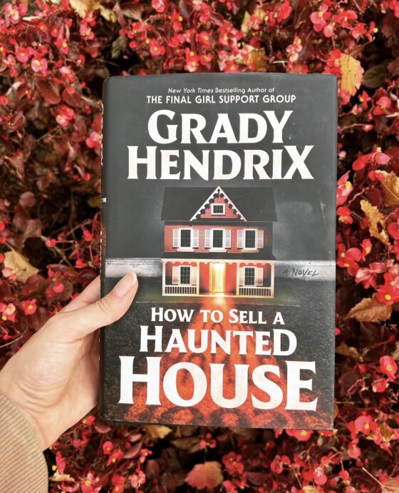 How to Sell a Haunted House held up in front of red flowers.