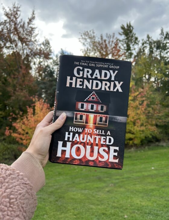 How to Sell a Haunted House held up in front of trees with different coloured leaves.