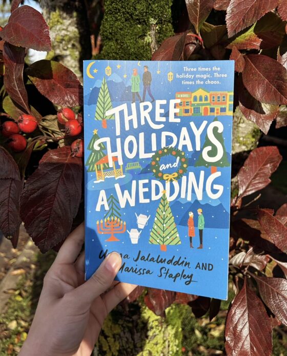 Three Holidays and a Wedding being held up in front of a tree with red leaves and berries.