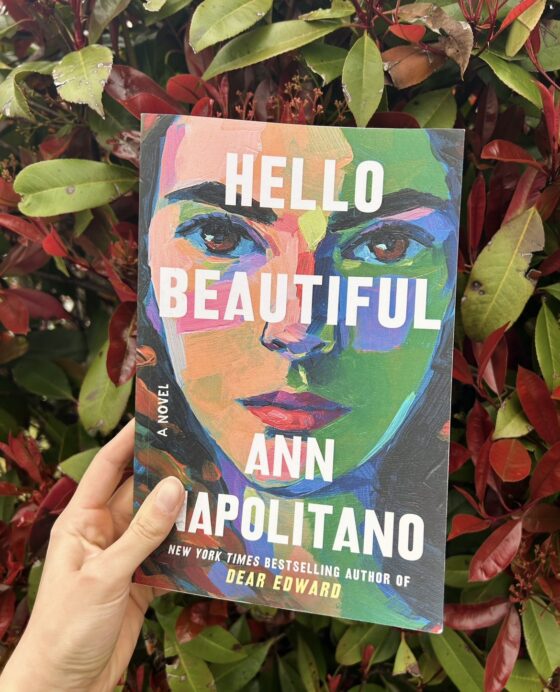 Hello Beautiful held in front of red and green bush.
